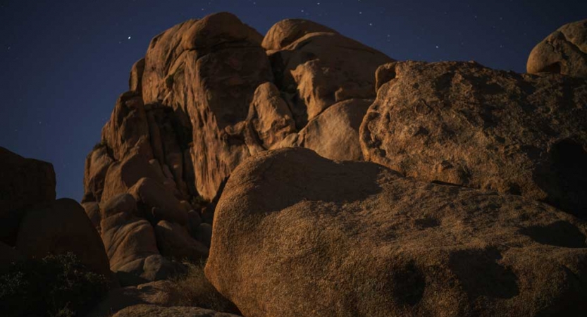 A large rock formation appears under a dark blue sky